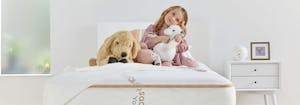 toddler sitting on top of big kid bed with stuffed animals