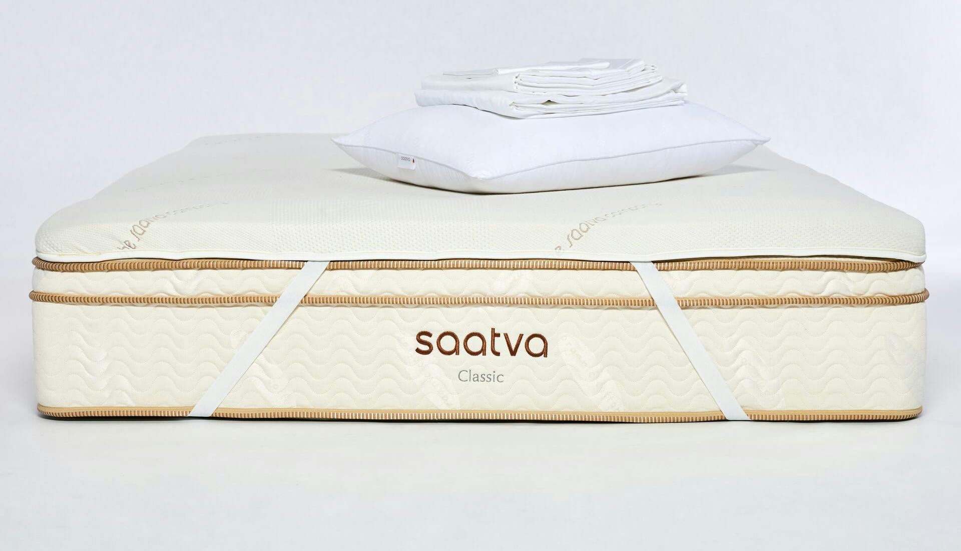 The Saatva Back-To-School Bedding Bundle which includes a memory foam mattress topper, a down alternative pillow, and the organic percale sheet set, all placed on an award-winning Saatva Classic Innerspring Mattress