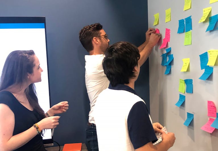 Three Saatva employees brainstorming around a whiteboard with colorful post-it notes