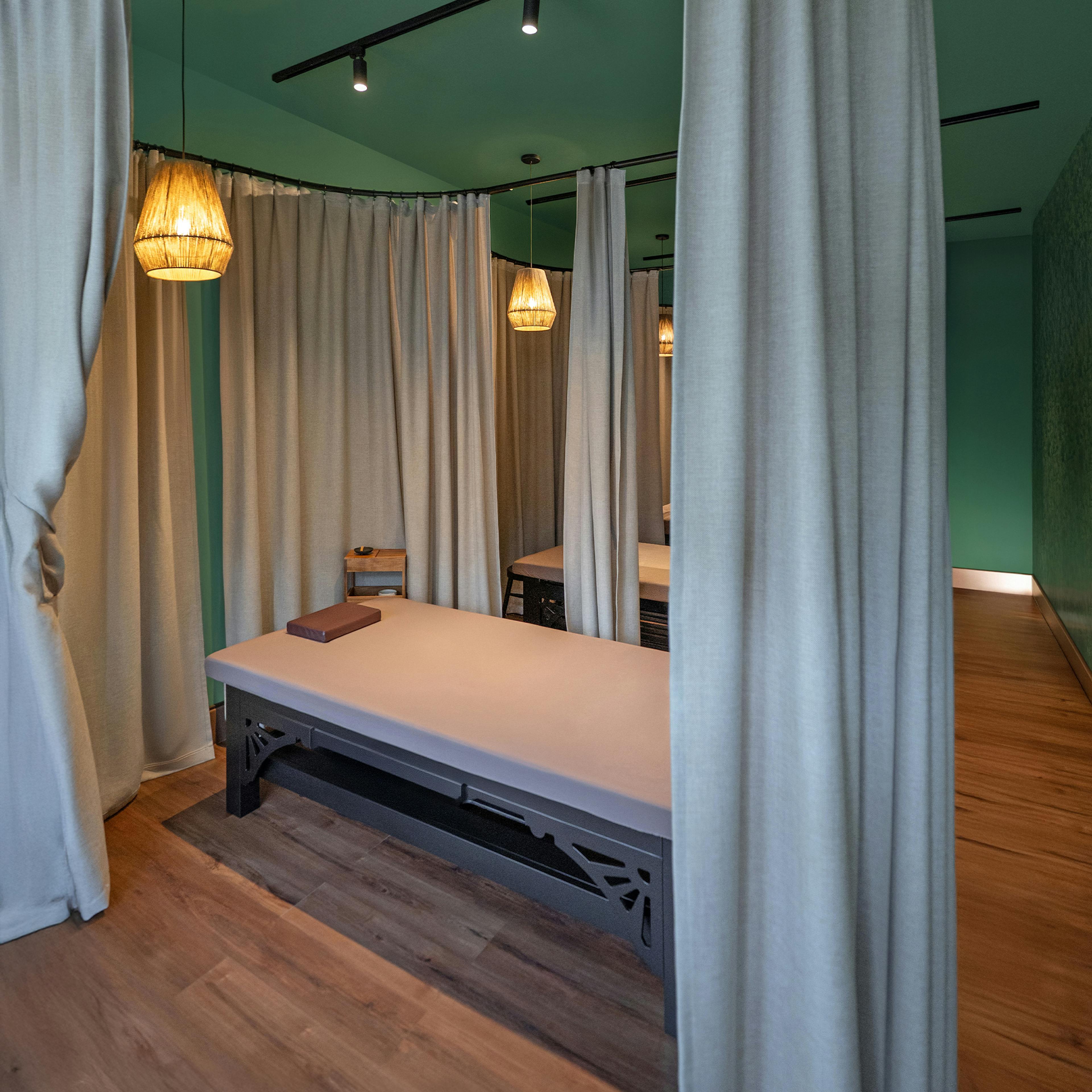 A massage room with canopy, wooden flooring, and ambient warm lighting.