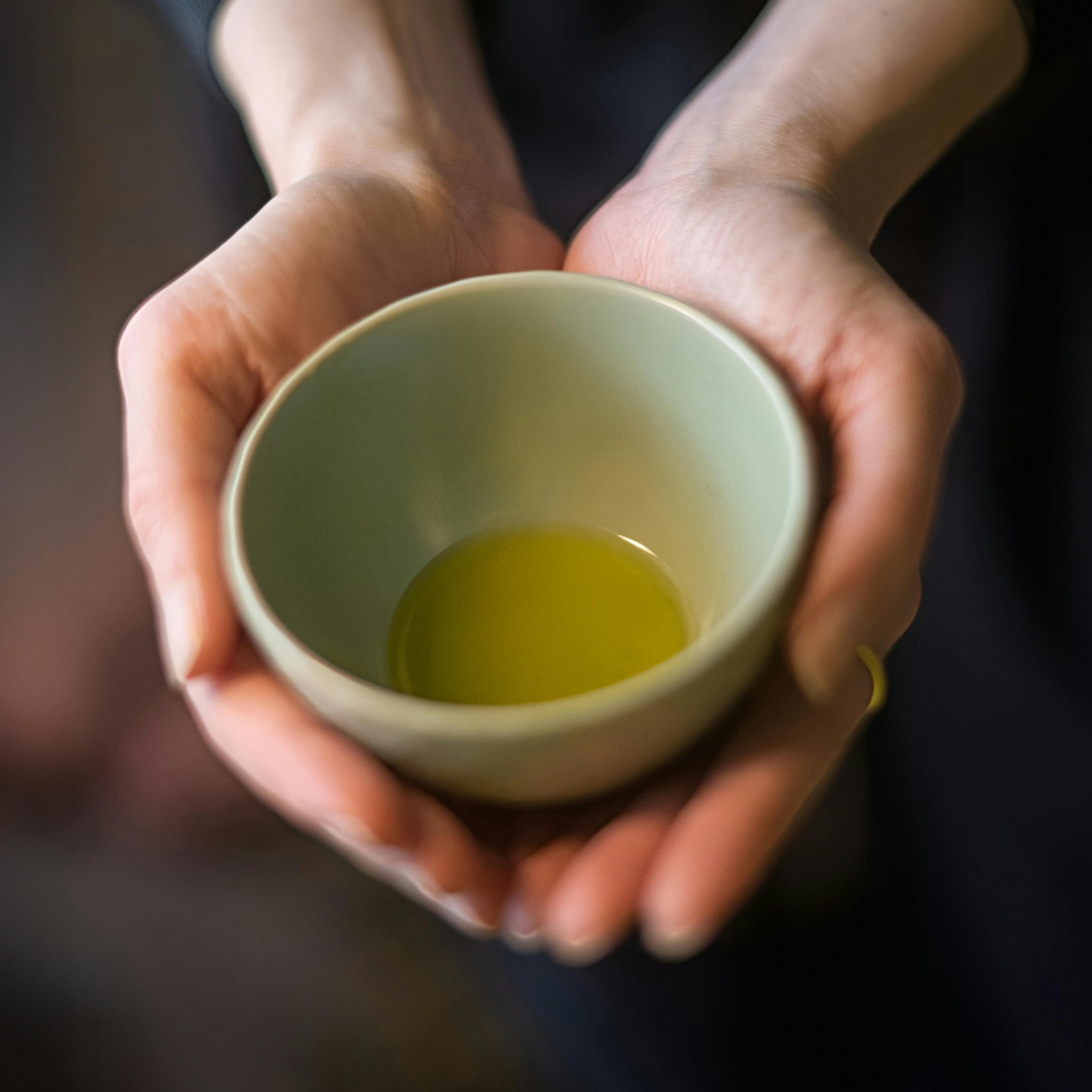 Therapist’s hands holding a small cup of warm massage oil: a symbol of intention and ritual.