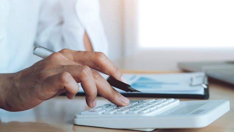 The hand of a man pressing numbers on a calculator at a desk