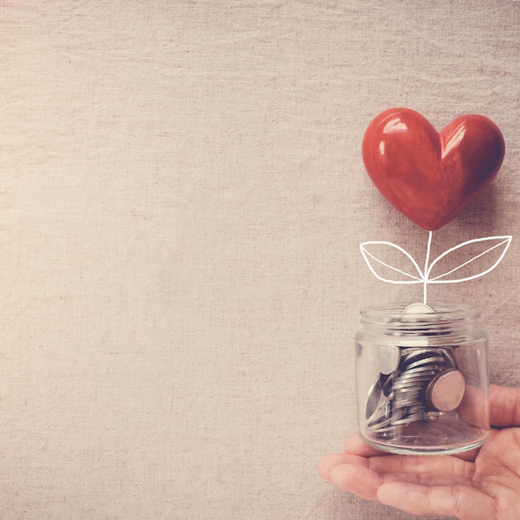Hand holding a jar of heart tree growing on money coins