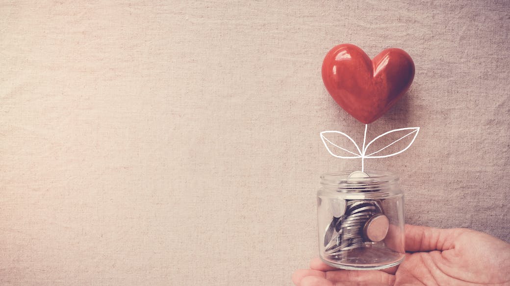 Hand holding a jar of heart tree growing on money coins