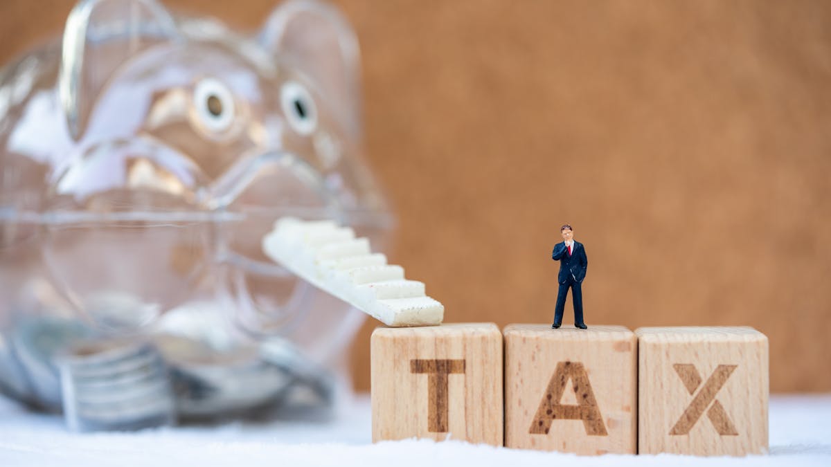 Bloques de letras en miniatura que deletrean TAX con una escalera mecánica que sube a una alcancía que está ahorrando dinero...