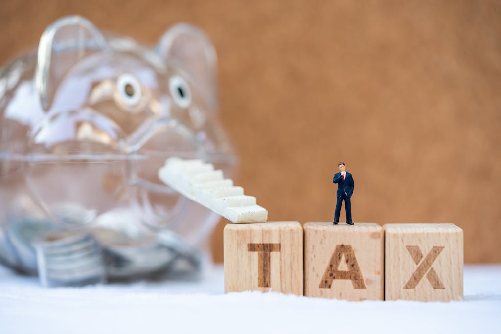 Miniature letter blocks that spell TAX with an escalator that steps up to a piggy bank that is saving money