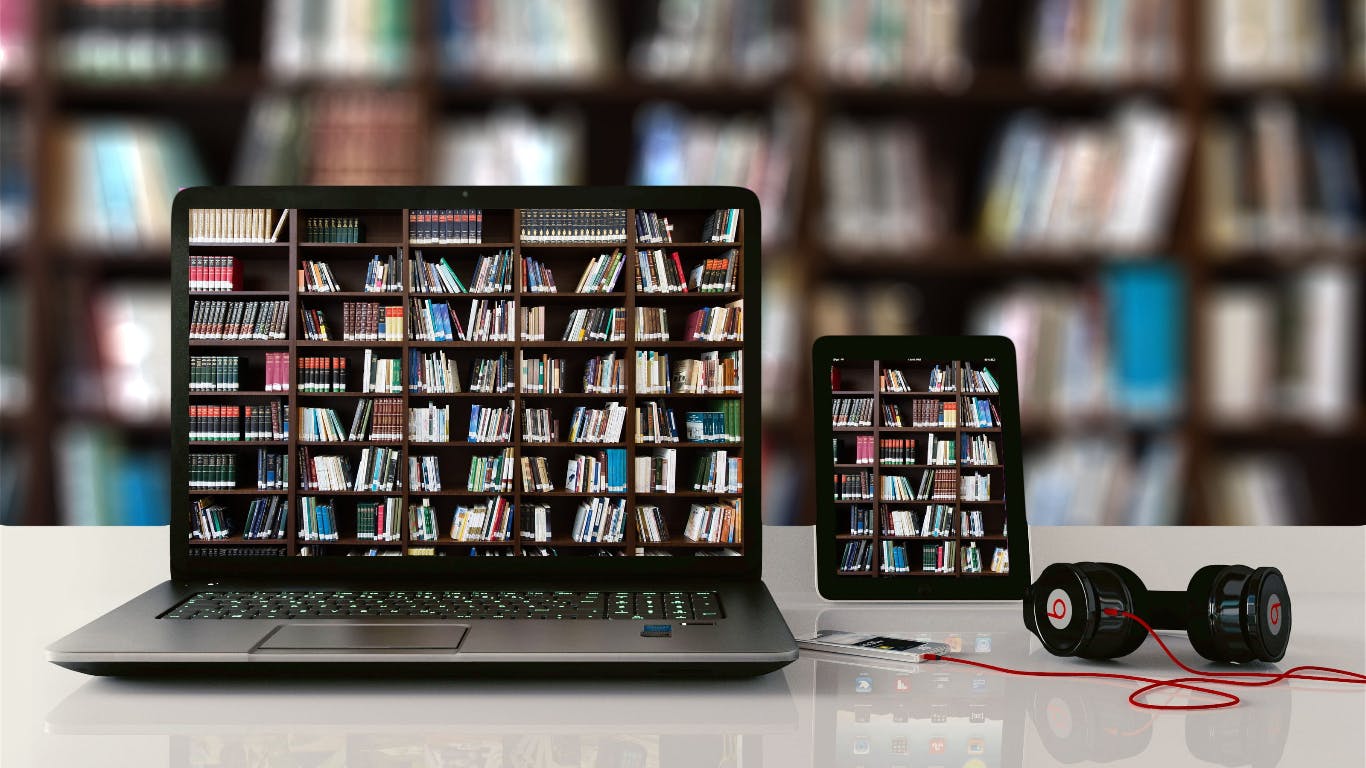 laptop and tablet in a library reflecting on a self full of books