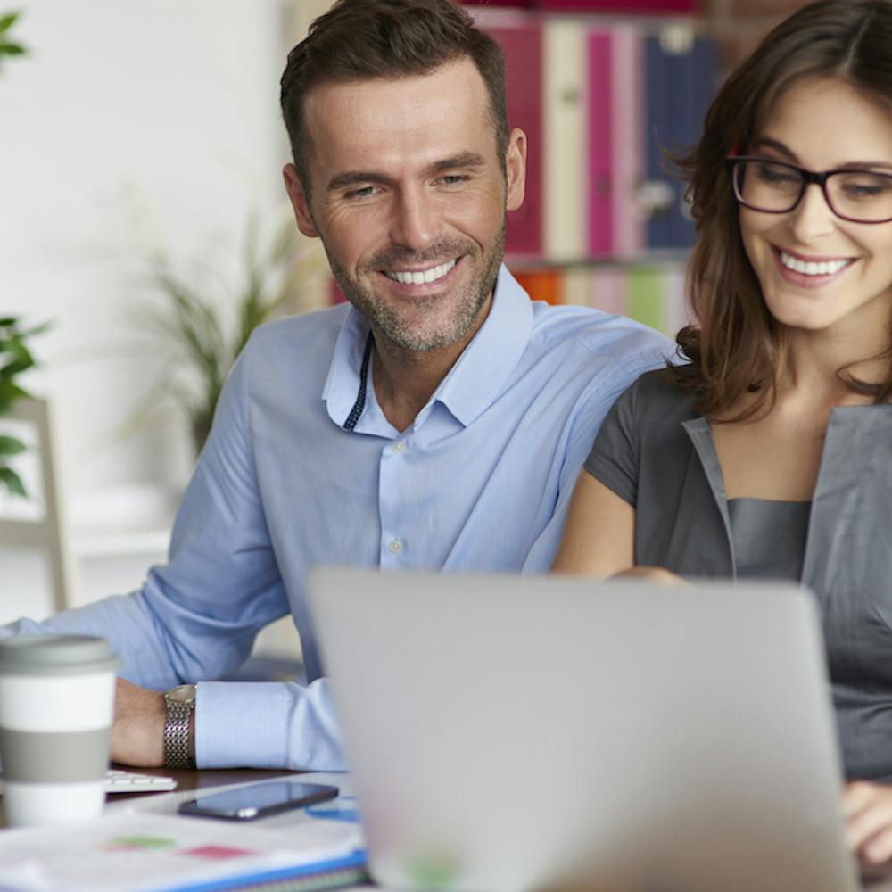 Happy Couple working together on their computers while smiling <a href="https://www.freepik.com/free-photo/close-up-people-working-office_13274141.htm#query=happy%20working%20couple&position=3&from_view=search&track=ais">Image by gpointstudio</a> on Freepik