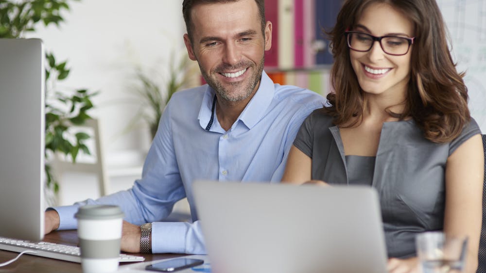 Happy Couple working together on their computers while smiling <a href="https://www.freepik.com/free-photo/close-up-people-working-office_13274141.htm#query=happy%20working%20couple&position=3&from_view=search&track=ais">Image by gpointstudio</a> on Freepik