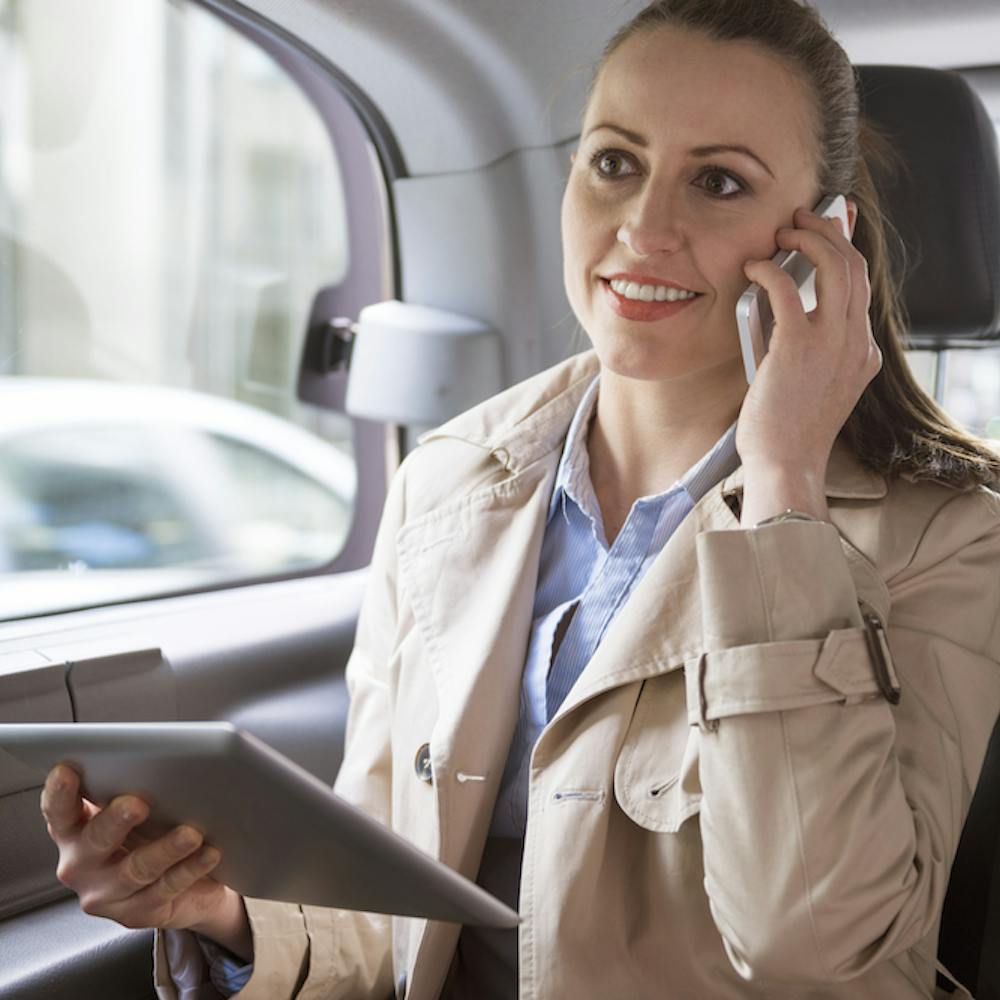 Woman making a phone call and using her tablet while seating the back seat of a car