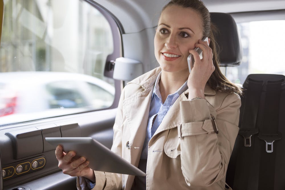 Woman making a phone call and using her tablet while seating the back seat of a car