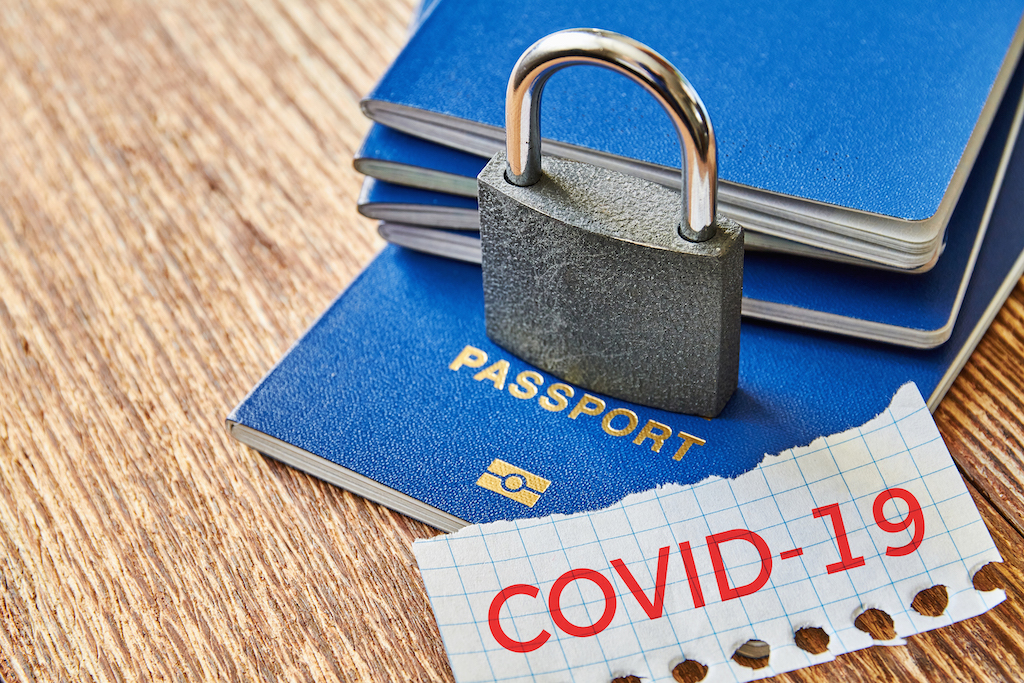 Stack of passports with a lock over them and a piece of paper with COVID-19 message