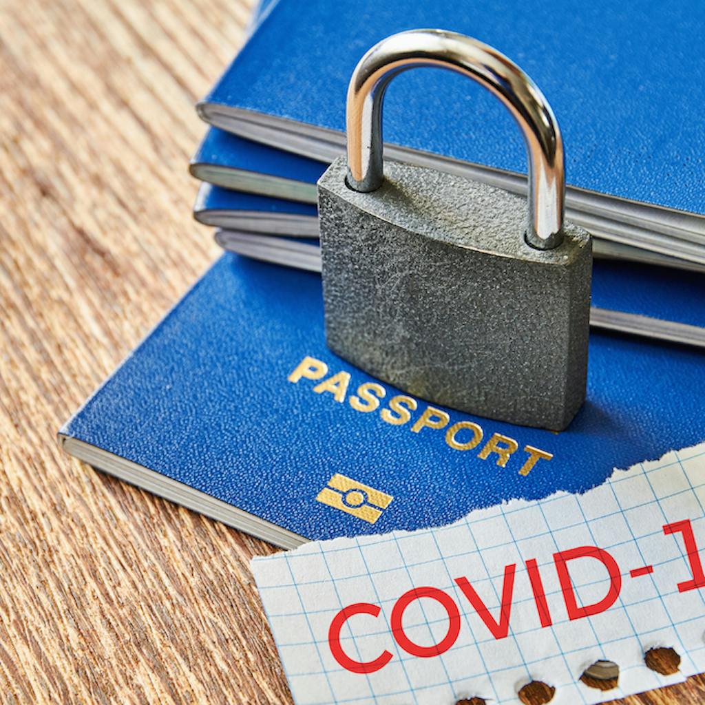 Stack of passports with a lock over them and a piece of paper with COVID-19 message