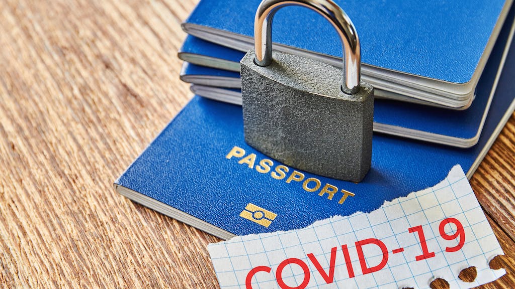 Stack of passports with a lock over them and a piece of paper with COVID-19 message