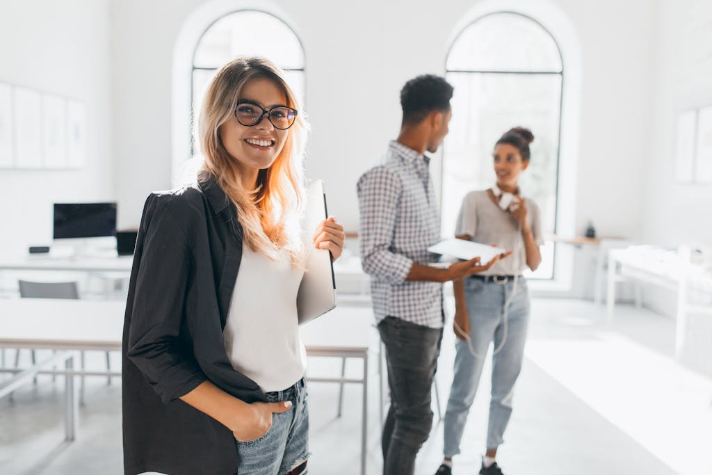 Elegant business-lady in trendy black jacket holding laptop and smiling in a modern looking office.