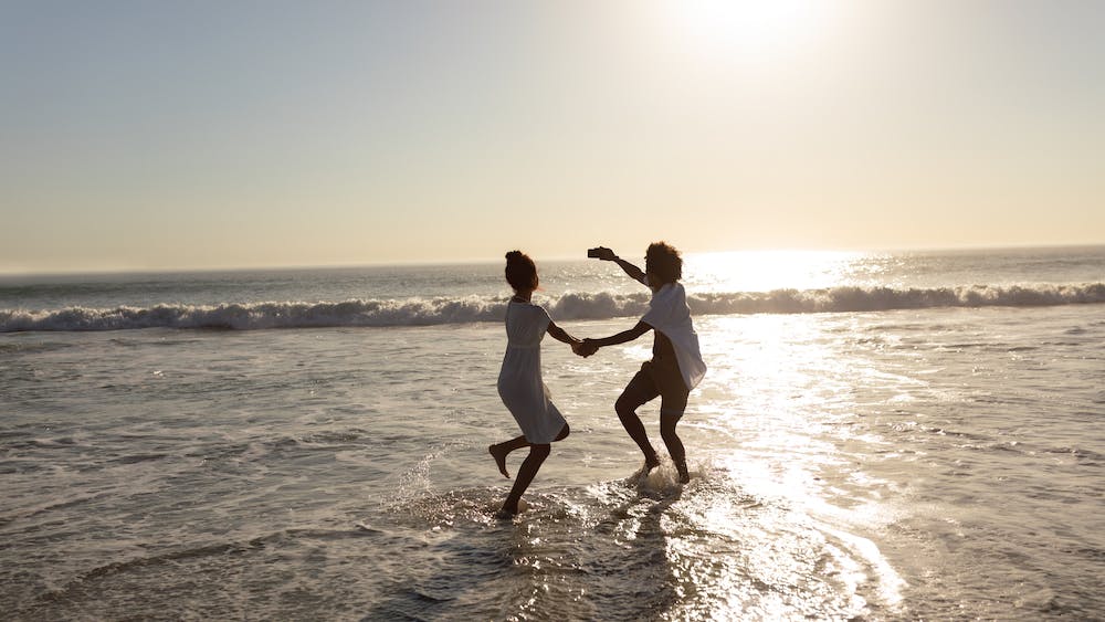 Photo of a couple having fun while dancing together on the beach <a href="https://www.freepik.com/free-photo/couple-having-fun-while-taking-selfie-with-mobile-phone-beach_5195151.htm#query=free%20happy%20beach&position=18&from_view=search&track=ais">Image by wavebreakmedia_micro</a> on Freepik