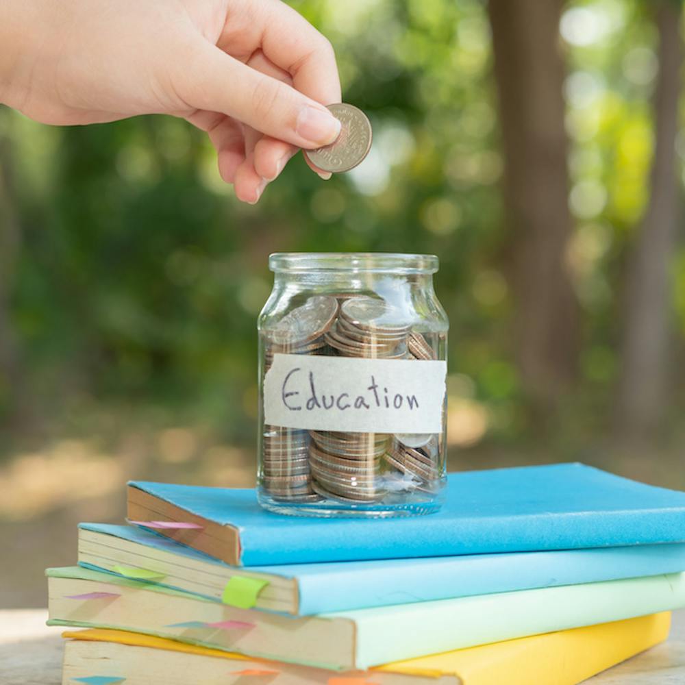 Photo of a hand putting money for savings in glass bottle for concept investment mutual fund finance and business, placed on textbooks. content money saving for ed<a href="https://www.freepik.com/free-photo/putting-money-coins-saving-glass-bottle-concept-investment-mutual-fund-finance-business-placed-textbook-content-money-saving-education_14779253.htm#query=college%20savings&position=48&from_view=search&track=ais">Image by jcomp</a> on Freepik