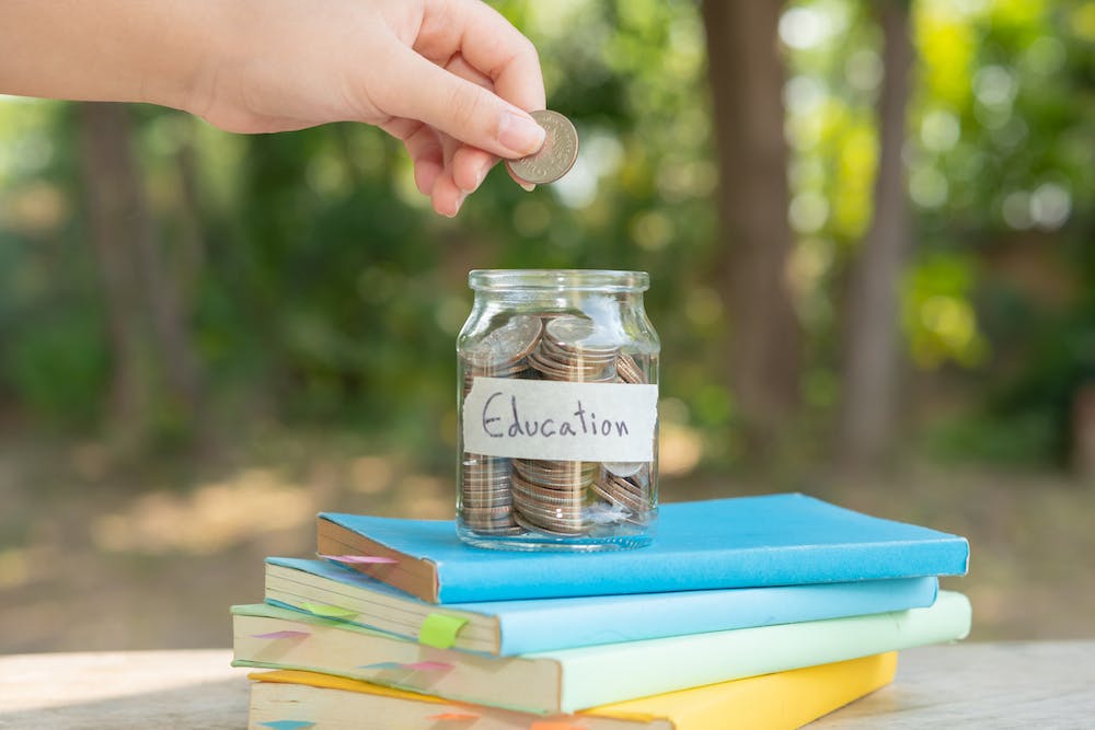 Photo of a hand putting money for savings in glass bottle for concept investment mutual fund finance and business, placed on textbooks. content money saving for ed<a href="https://www.freepik.com/free-photo/putting-money-coins-saving-glass-bottle-concept-investment-mutual-fund-finance-business-placed-textbook-content-money-saving-education_14779253.htm#query=college%20savings&position=48&from_view=search&track=ais">Image by jcomp</a> on Freepik