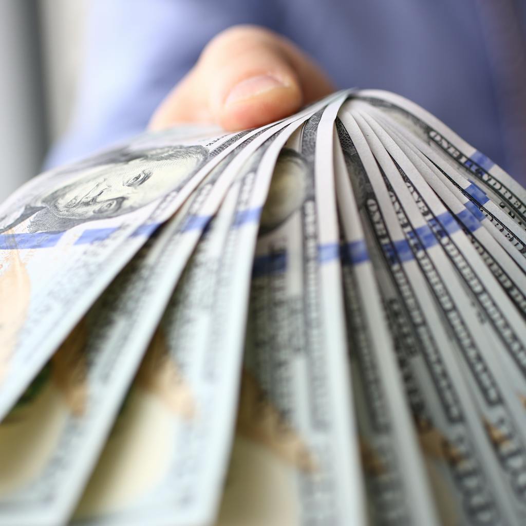 Man in suit and tie hold in arm pack of hundred of dollars