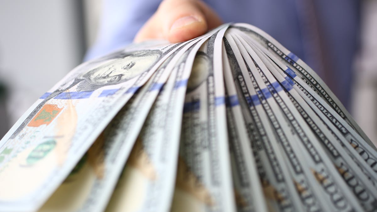 Man in suit and tie hold in arm pack of hundred of dollars