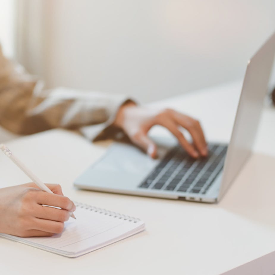 Businesswoman typing on laptop and writing on notebook