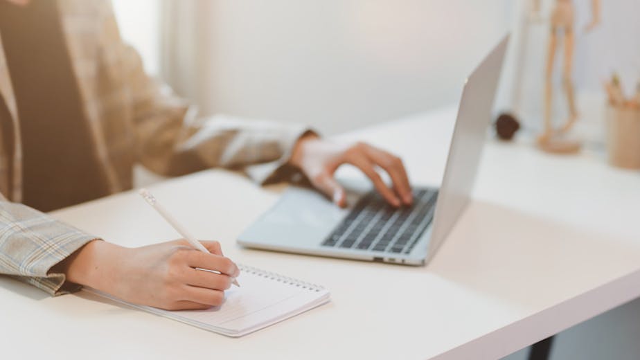 Businesswoman typing on laptop and writing on notebook