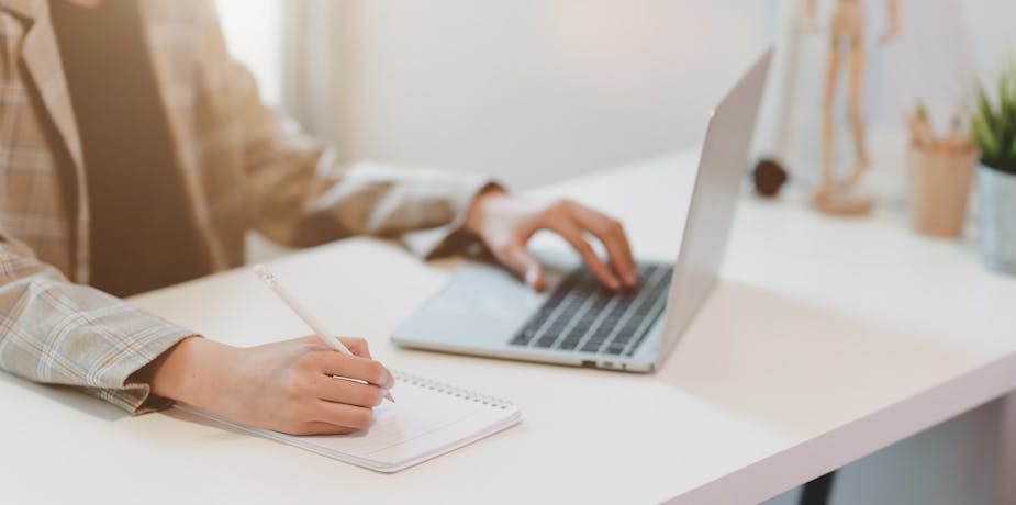Businesswoman typing on laptop and writing on notebook