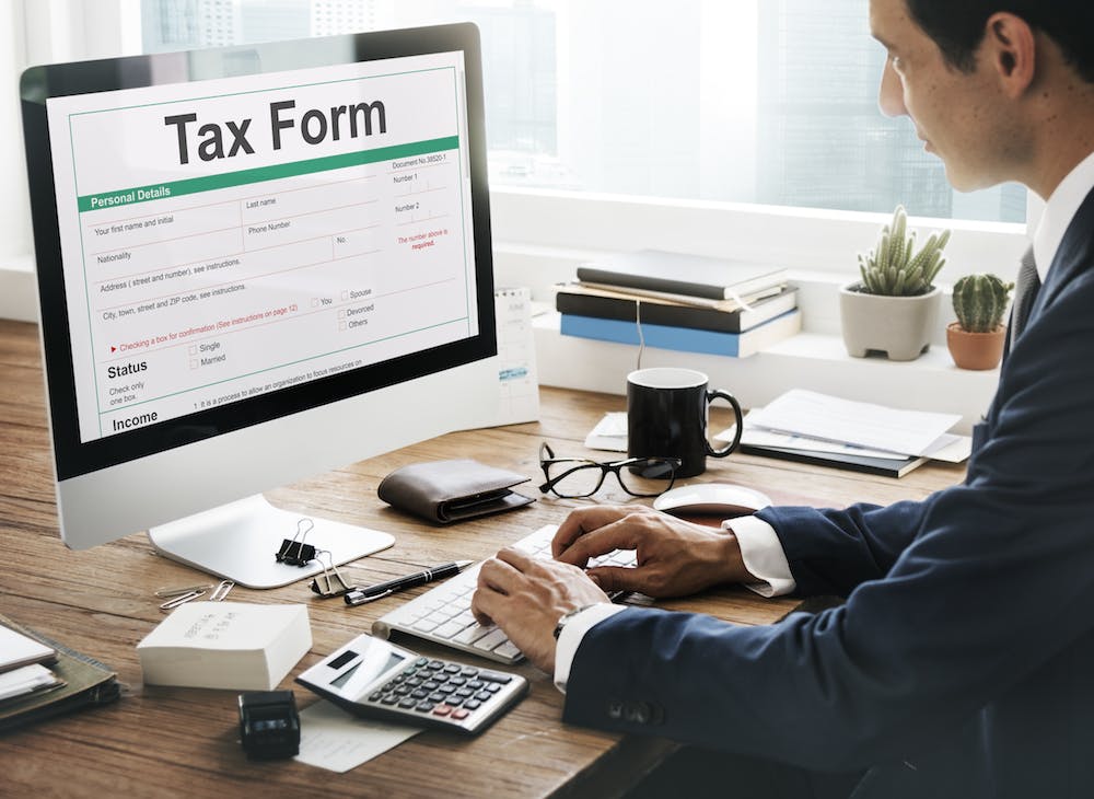 Young man sitting on his desk working on his computer filling out his tax form <a href="https://www.freepik.com/free-photo/tax-credits-claim-return-deduction-refund-concept_16470144.htm#query=taxes&position=49&from_view=search&track=sph">Image by rawpixel.com</a> on Freepik