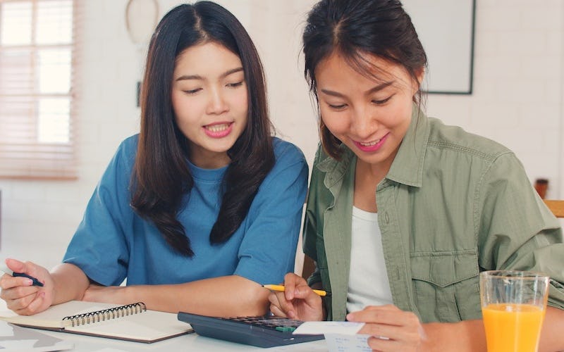 Two women smile while taking notes and looking at a calculator