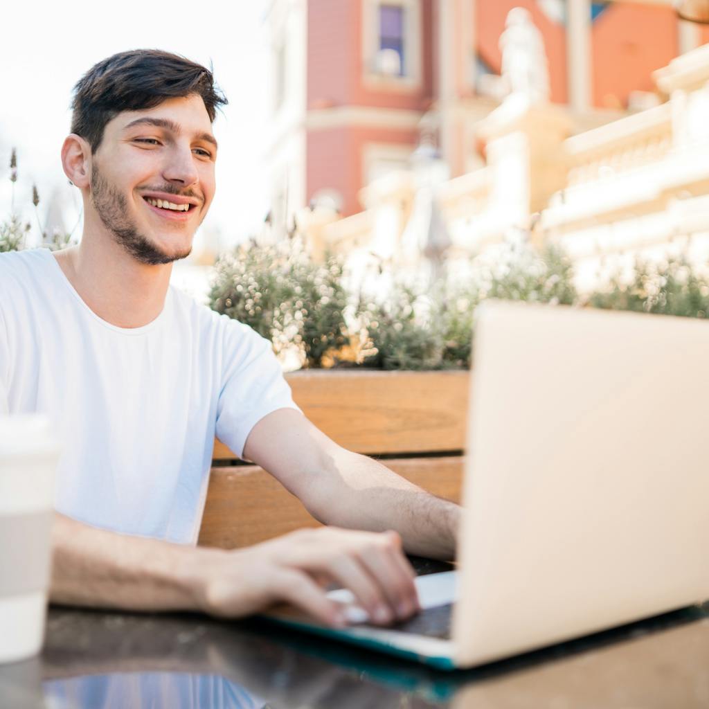 Portrait of young man using his laptop while sitting in an open-air coffee shop. Technology and lifestyle concept