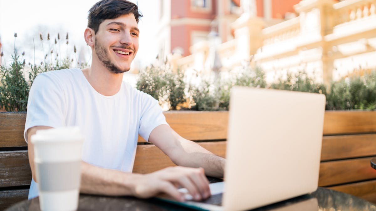 Portrait of young man using his laptop while sitting in an open-air coffee shop. Technology and lifestyle concept