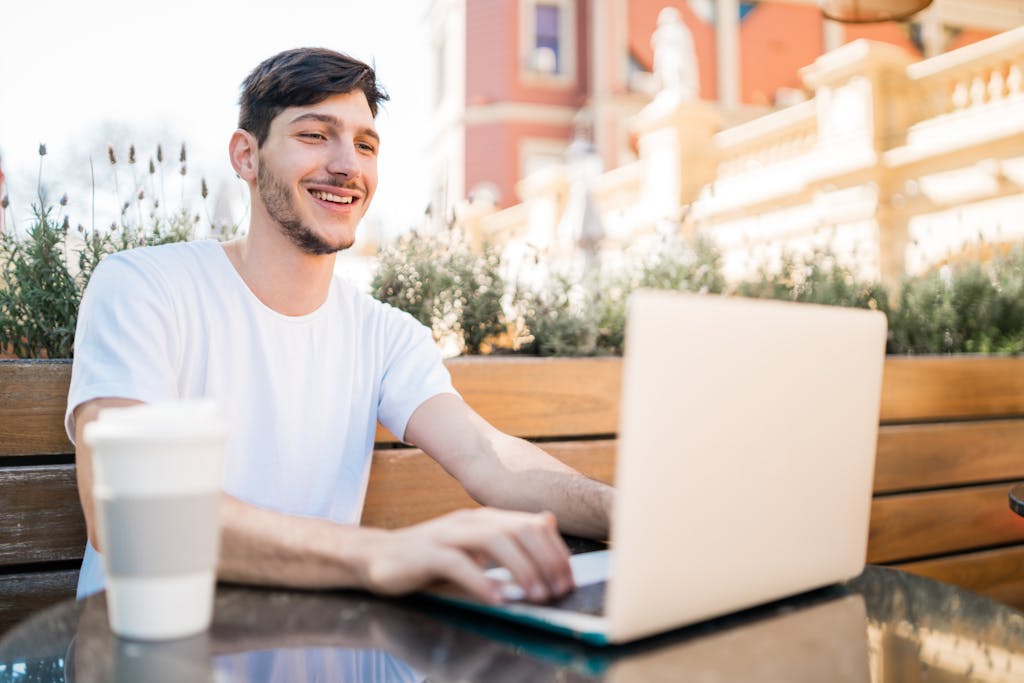 Portrait of young man using his laptop while sitting in an open-air coffee shop. Technology and lifestyle concept