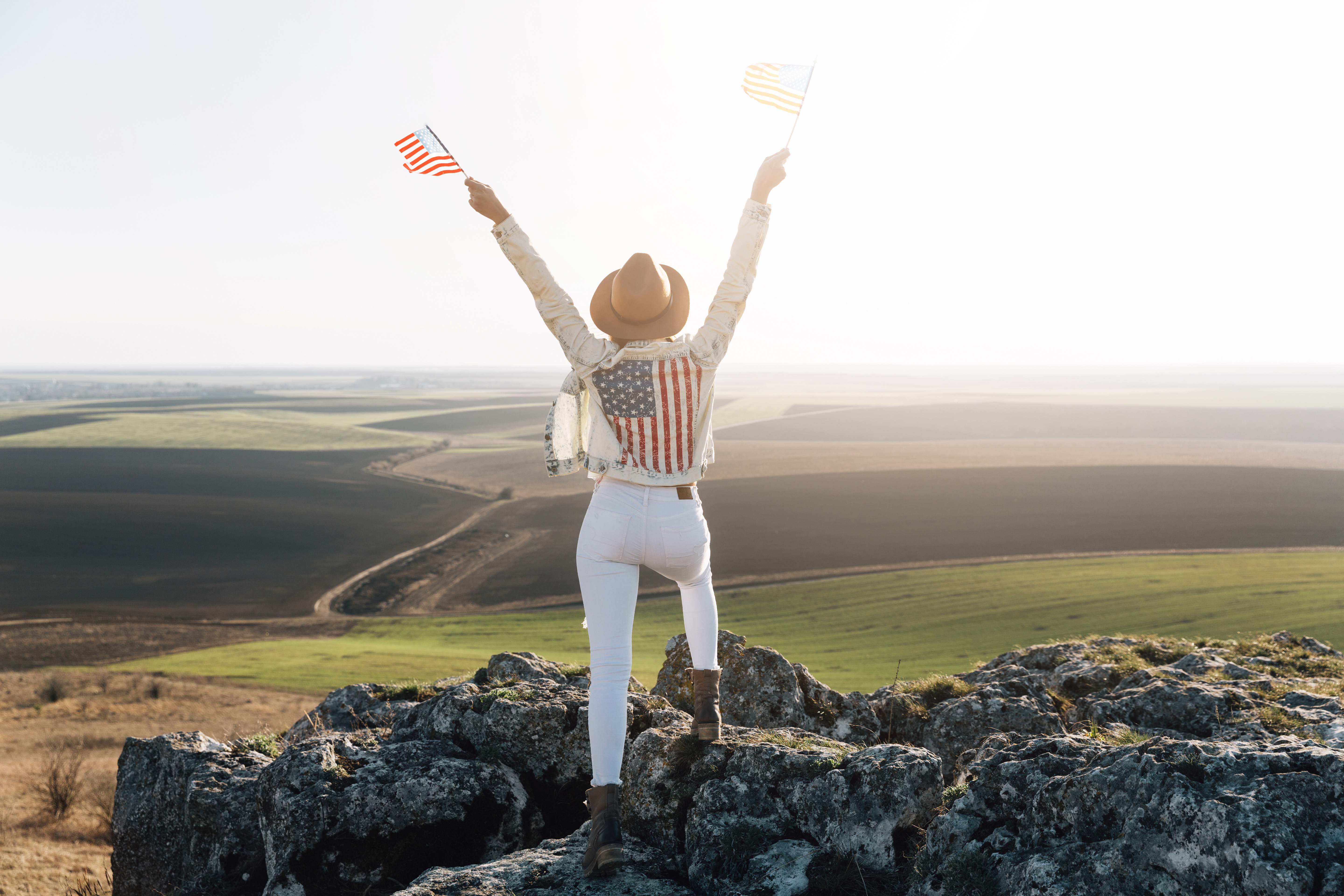 Patriotic woman posing with American flags on top of mountain