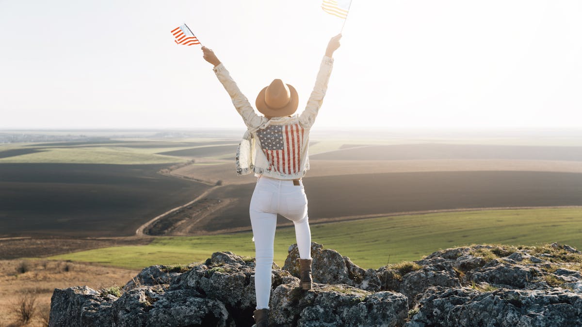 Patriotic woman posing with American flags on top of mountain