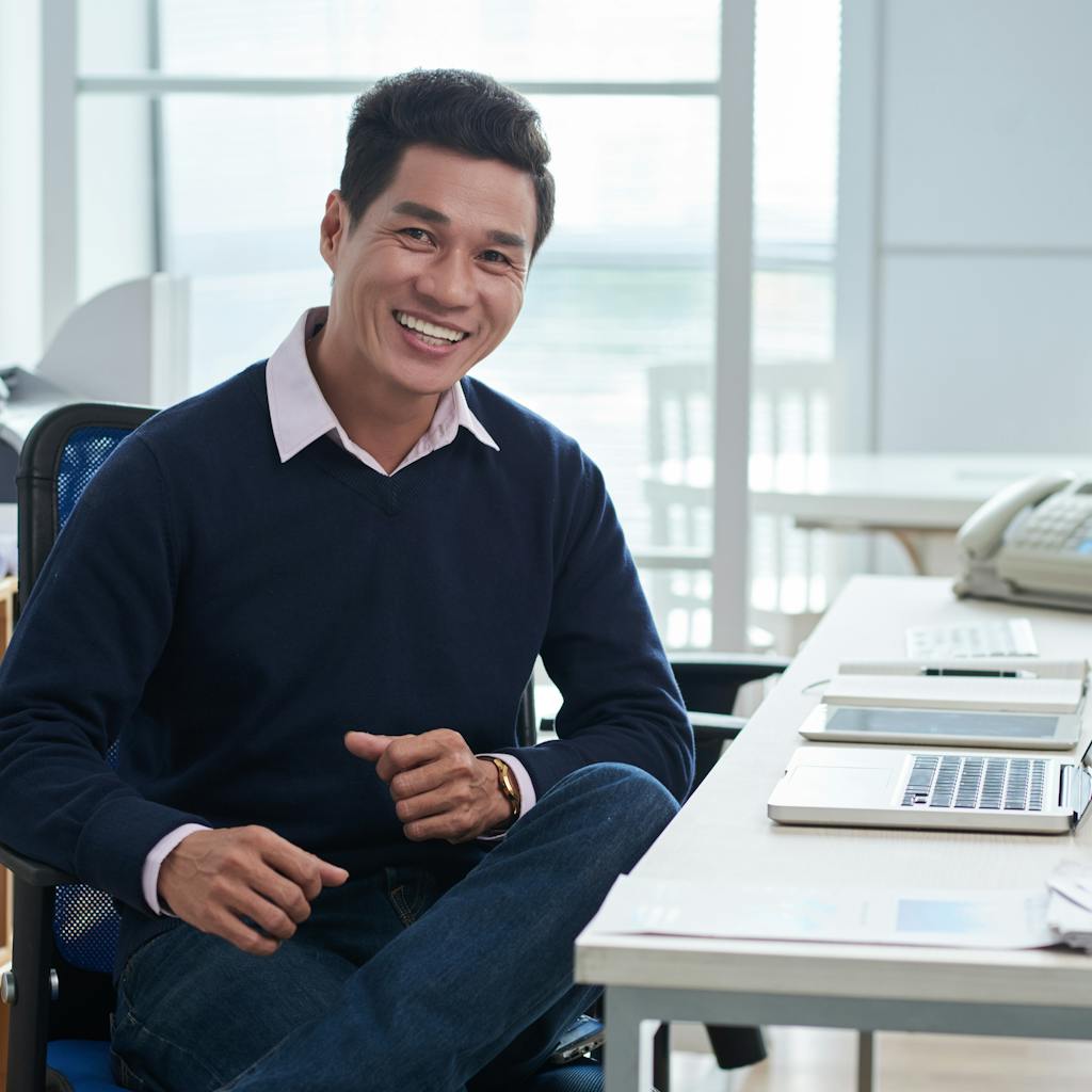 Smiling man sitting at desk in front of laptop in office and looking at camera