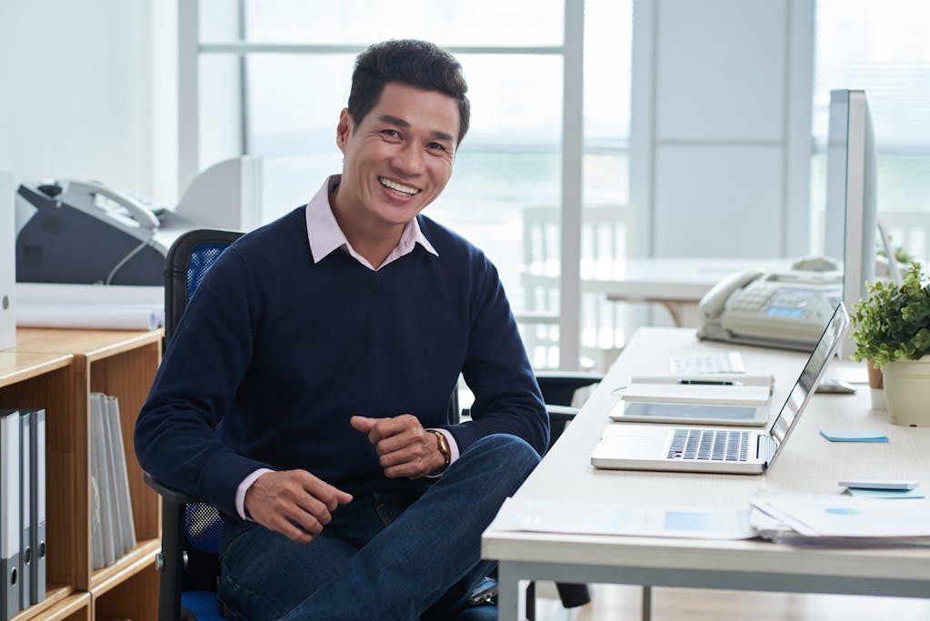 Smiling man sitting at desk in front of laptop in office and looking at camera