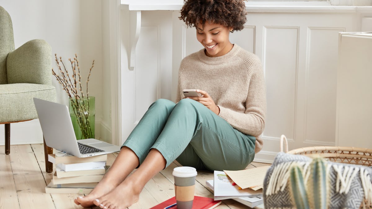 Positive young woman with afro haircut, dressed in fashionable clothes looking at her cell phone while smiling. <a href='https://www.freepik.com/photos/coffee'>Coffee photo created by wayhomestudio - www.freepik.com</a>