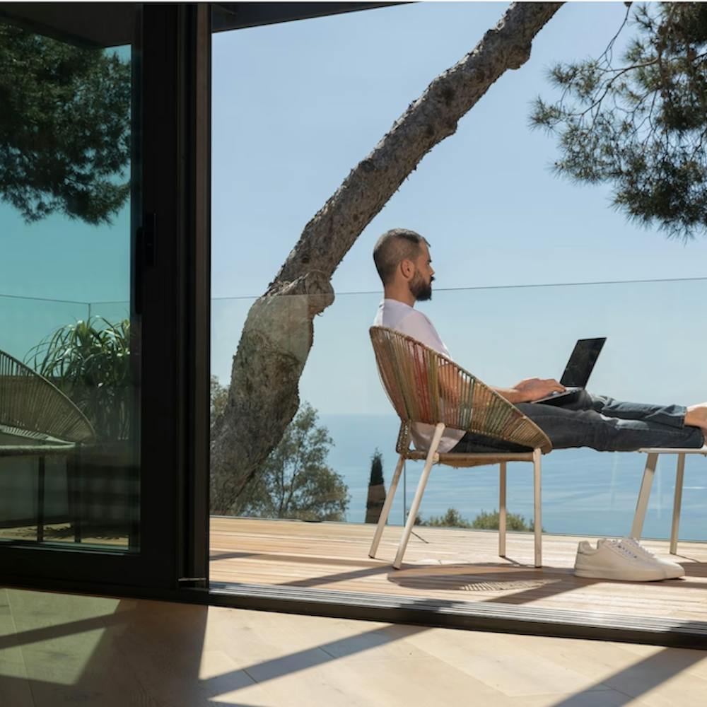 Man working outdoors overlooking the sea from a glass balcony. Image by <a href="https://www.freepik.com/free-photo/full-shot-man-working-outdoors_13658999.htm#query=puerto%20rico%20remote%20work&position=10&from_view=search&track=ais">Freepik</a>