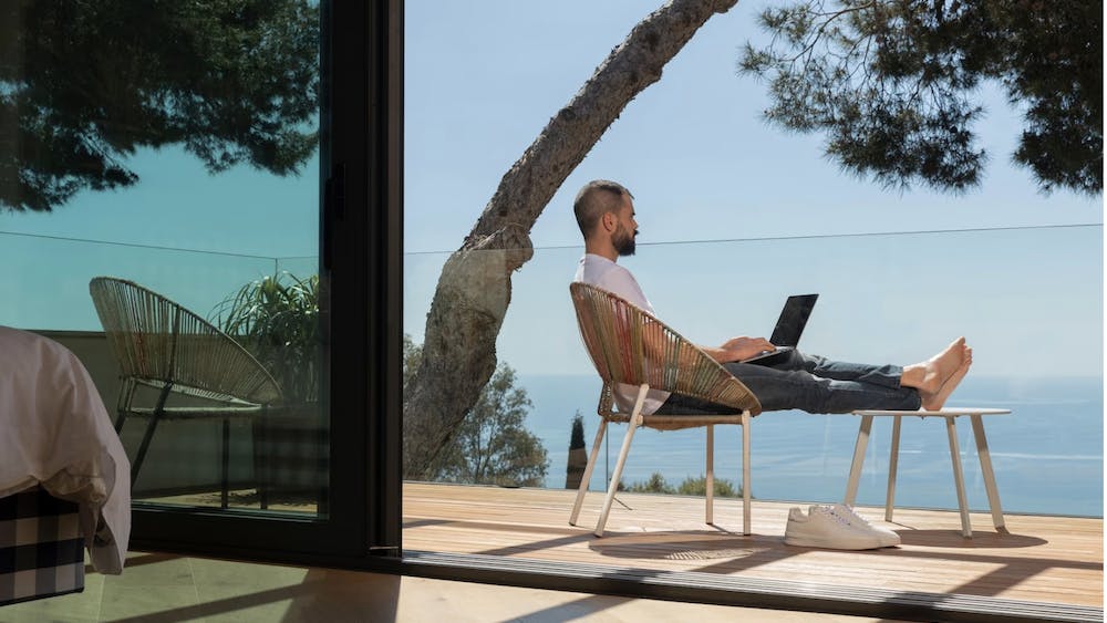 Man working outdoors overlooking the sea from a glass balcony. Image by <a href="https://www.freepik.com/free-photo/full-shot-man-working-outdoors_13658999.htm#query=puerto%20rico%20remote%20work&position=10&from_view=search&track=ais">Freepik</a>