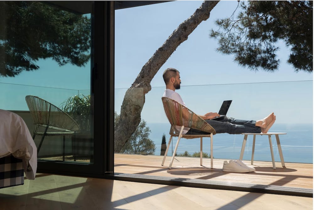 Man working outdoors overlooking the sea from a glass balcony. Image by <a href="https://www.freepik.com/free-photo/full-shot-man-working-outdoors_13658999.htm#query=puerto%20rico%20remote%20work&position=10&from_view=search&track=ais">Freepik</a>