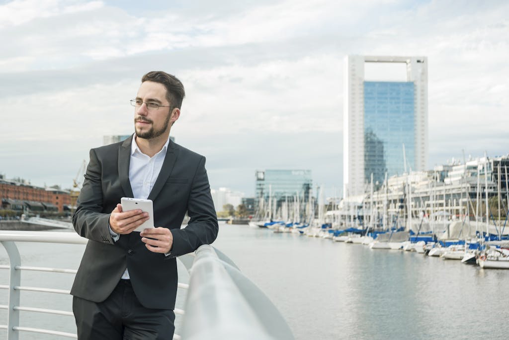 Portrait of a young businessman standing near the harbor holding mobile phone