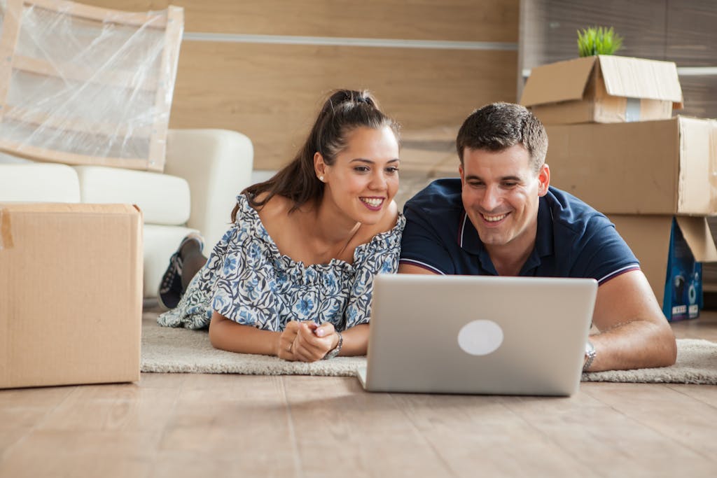 Husband and wife on their laptop in the living room of their home surrounded by moving boxes