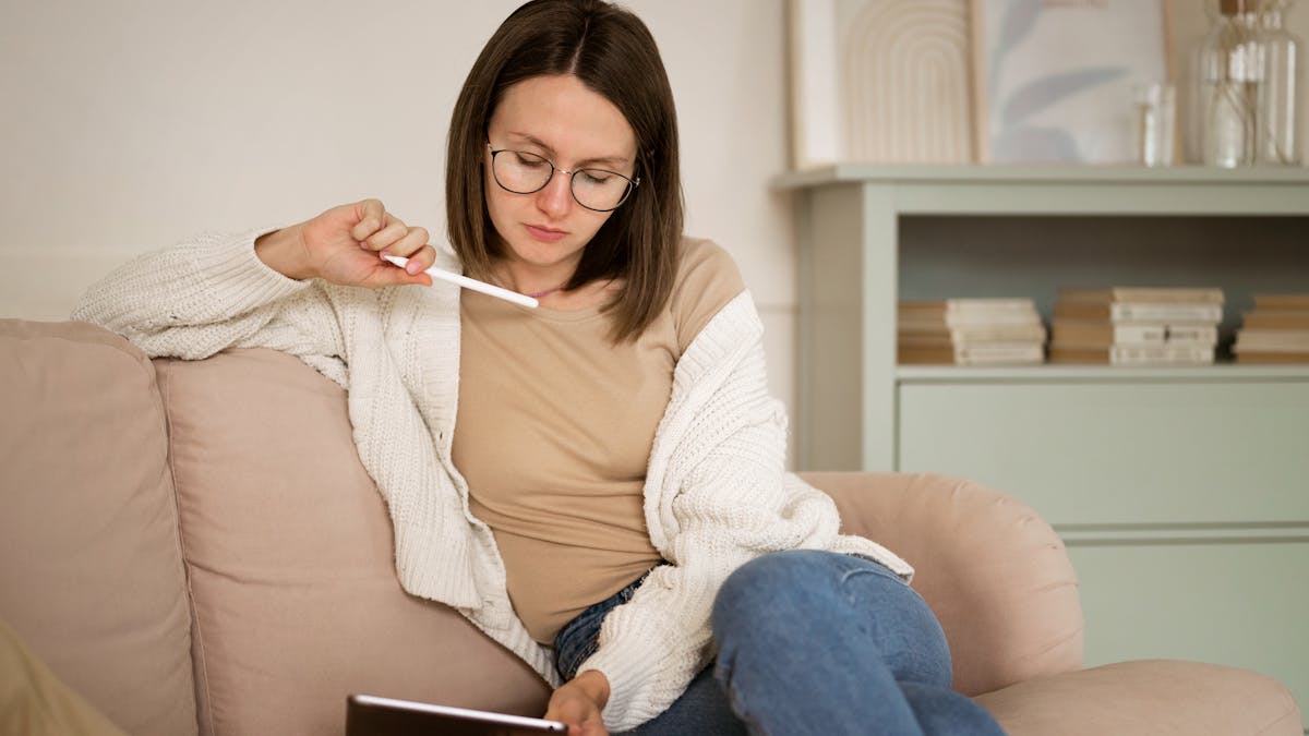 Mujer sentada en su sofá pensando y trabajando en su tablet