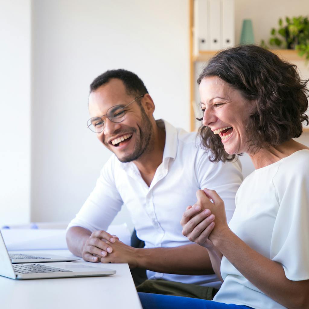 Pareja feliz se ríe mientras leen frente a su computadora