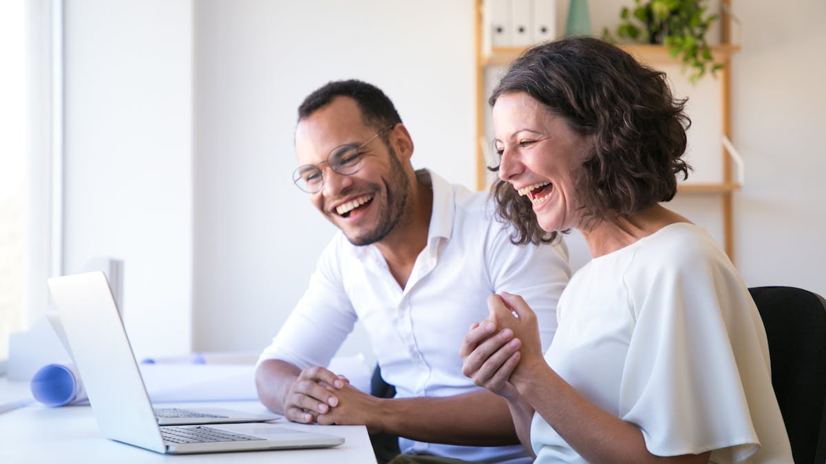 Pareja feliz se ríe mientras leen frente a su computadora
