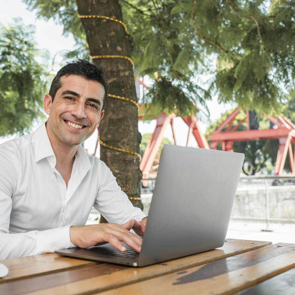 Joven emprendedor sonriendo al aire libre mientras trabaja en su computadora portátil