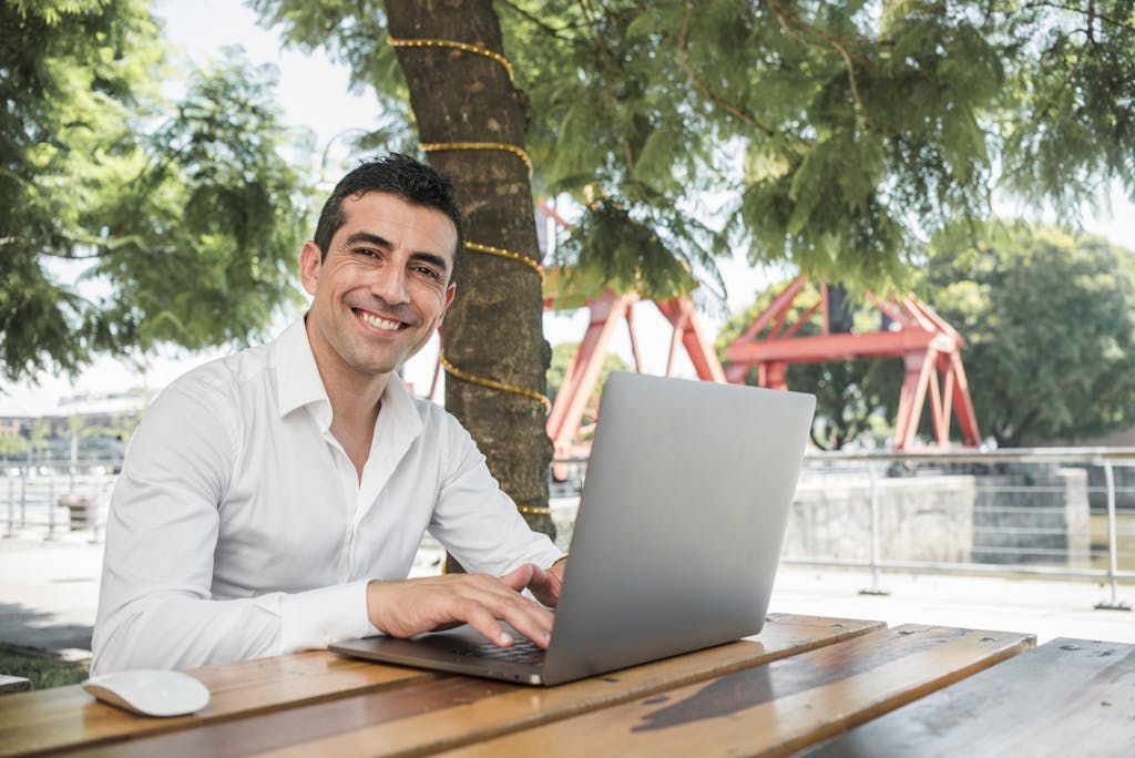Young entrepreneur man smiling outdoors while working from his laptop