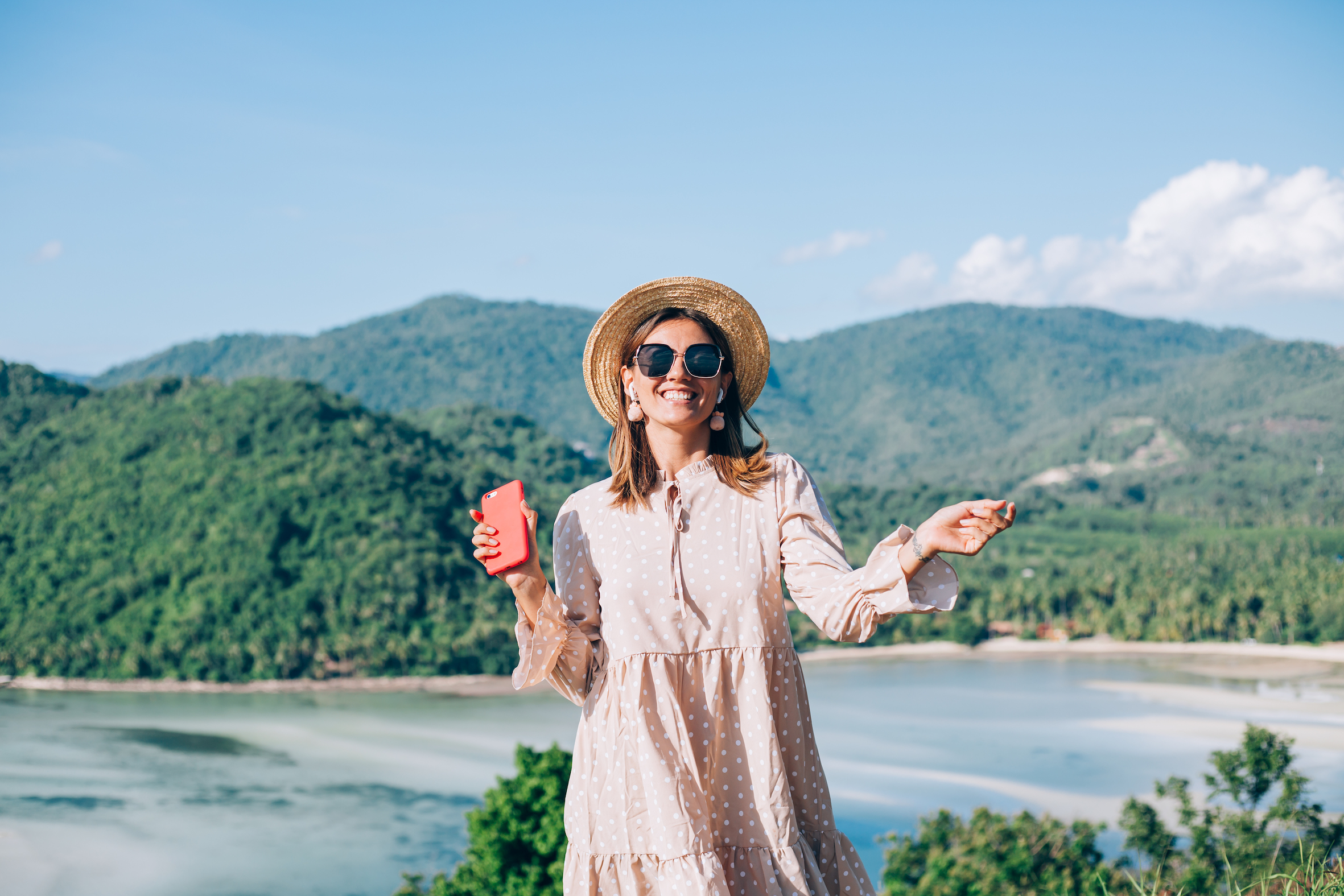 Young woman in summer cute dress, straw hat and sunglasses dancing with smartphone on hand