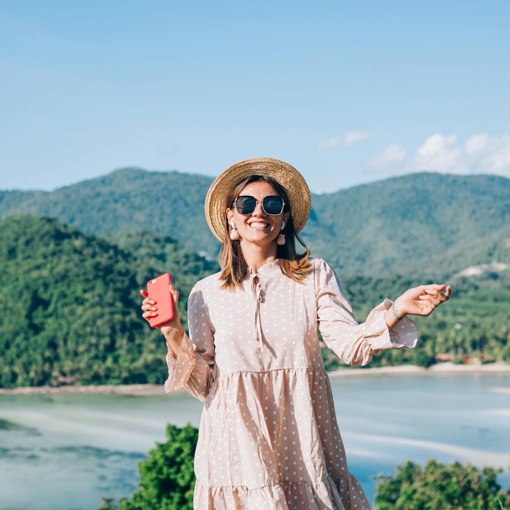 Young woman in summer cute dress, straw hat and sunglasses dancing with smartphone on hand