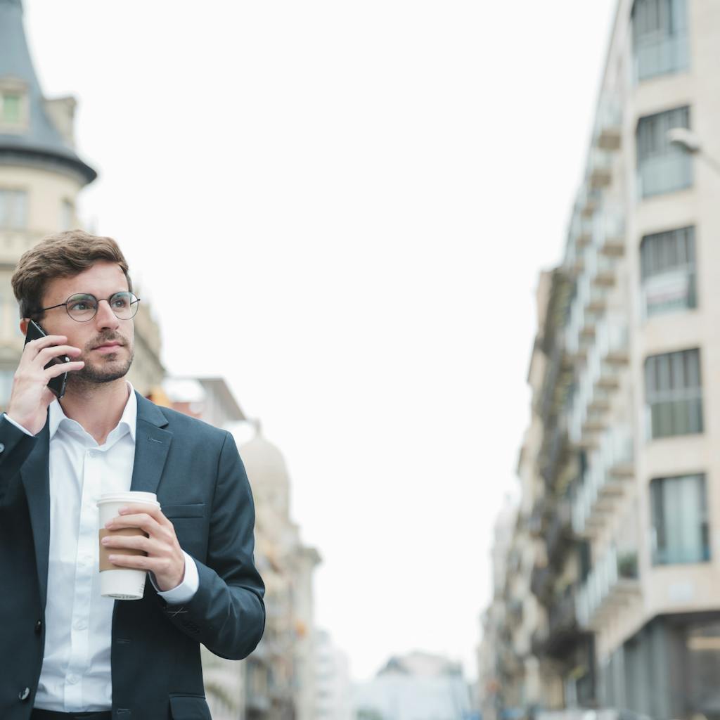 Businessman holding standing on street holding takeaway coffee cup in hand talking on mobile phone